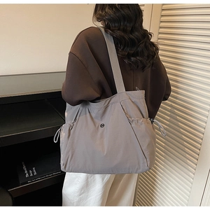 Rear view of model wearing a grey nylon large capacity tote bag with drawstring side pocket