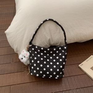 Détail d'un sac cabas noir à pois avec pendentif chien en peluche sur coussin blanc
