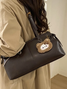 Vintage dark brown leather tote bag with plush bear charm worn by a model in a trench coat