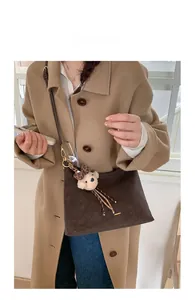 Detail of dark brown suede crossbody bag with plush bear charm and leather strap