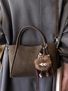Brown textured top-handle crossbody bag with cute plush monster charm and sleek strap