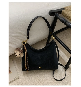 Detail of black suede hobo bag with contrast stitching and teddy bear charm