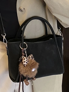 Elegant black suede handbag with plush bear charm and detachable crossbody strap