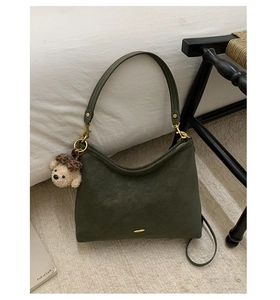 Detail of olive green textured shoulder bag featuring a cute plush bear charm with bow