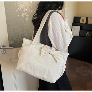 Side view of an oversized cream tote bag with a large ribbon bow and elastic side pockets