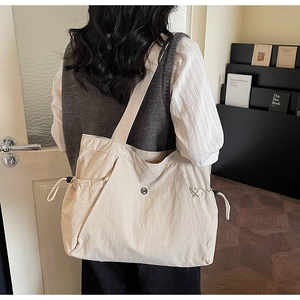 Detail of large beige tote bag with drawstring side and metallic logo for daily use