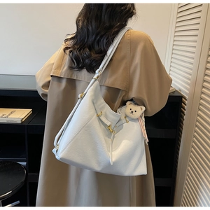 Detail view of large white tote bag with bear charm worn with khaki trench coat