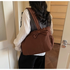 Detail of dark brown tote bag featuring a large bow and side drawstring pocket