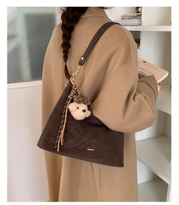 Detailed view of dark brown crescent bag with plush bear charm and leather tassels