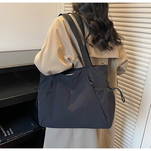 Detail of black nylon tote bag featuring side drawstring pocket and metal logo detail