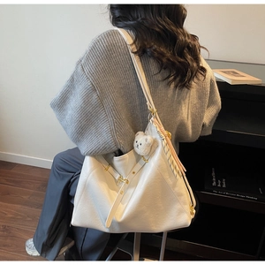 Detail view of large white tote bag with cute plush bear charm on a model shoulder