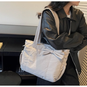 Detailed view of grey tote bag featuring a large decorative bow and side pleated pockets