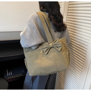 Detail of olive green quilted tote bag with large bow and side pockets on soft sweater