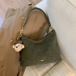 Close-up of a dark green suede crescent bag featuring gold hardware and a cute puppy charm