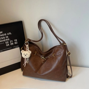Detail of a brown leather tote bag with gold hardware and a cute white plush bear pendant