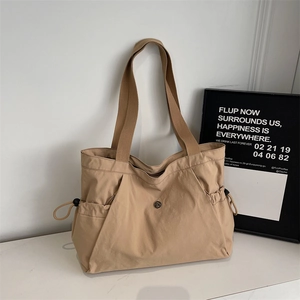 Detail shot of khaki tote bag featuring side drawstring pockets and metallic logo plaque