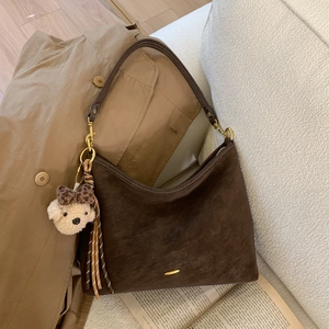 Deep brown matte suede half-moon bag with cute bear charm and tassel on autumn trench coat