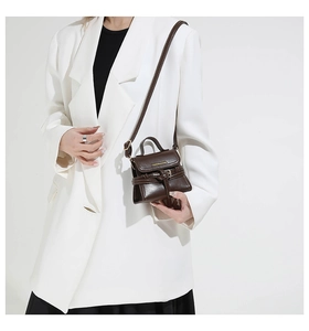 Detailed close-up of dark brown leather square bag featuring elegant gold logo and handle
