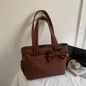 Detail of brown canvas tote bag with bow decoration and side pockets in a lifestyle setting