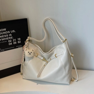Detail view of cream-white tote bag with golden metal ring and plush bear charm accessory