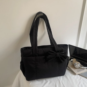 Detail of black quilted tote bag with large bow and side pockets on a desk