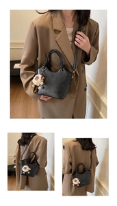 Detail of a black matte leather bucket bag with gold accents and a white sheep plush charm