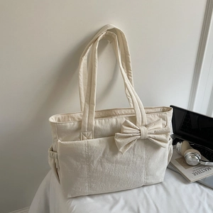 Detail of cream canvas tote bag featuring large bow decoration and side drawstring pockets
