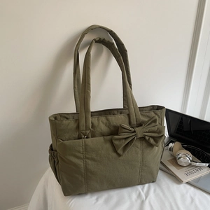 Detail of olive green quilted tote bag featuring a large bow and functional side pockets