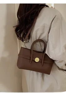 Detailed view of the brown leather texture and vintage gold circular lock on the handbag