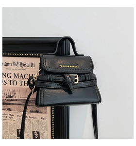 Close-up of black PU leather mini square bag with strap against vintage newspaper background