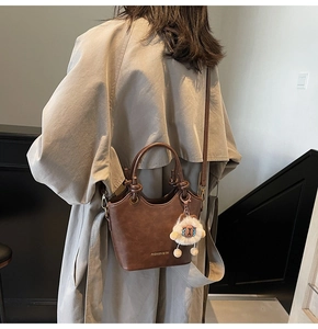 Detail view of dark brown leather bucket bag with a cute sheep charm and long strap