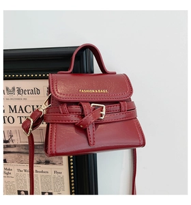 Detail of a dark red textured leather mini bag with gold hardware and fashion lettering