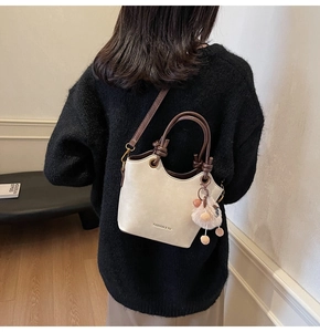 Detail of a chic cream bucket bag with brown handles and a plush charm on a model