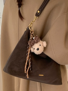 Brown suede shoulder bag with plush bear charm and woven tassel on winter coat