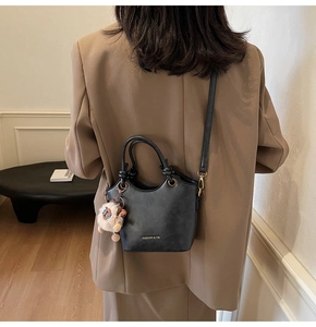 Detail of black matte leather bucket bag with knot handle and lion plush charm on model
