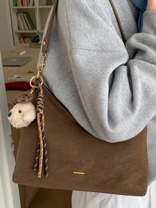 Brown suede tote bag with gold hardware and plush charm shown on female model