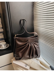 Gros plan sur la texture en cuir marron foncé plissé et la plaque de marque du sac