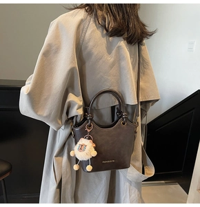 Detail of dark brown bucket bag with plush sheep charm and gold brand logo on matte leather