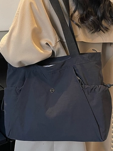 Minimalist black nylon large capacity tote bag worn by a model in a khaki trench coat