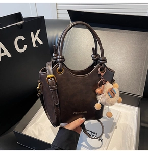 Detail of dark brown leather handbag with knotted handle and alpaca charm on a gift box