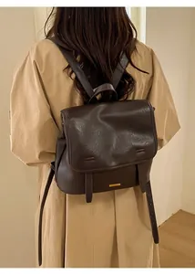 Zaino vintage in pelle marrone scuro con fibbia a patta mostrato su una modella in trench-coat