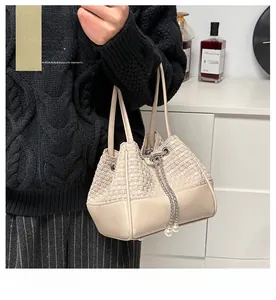 Detailed shot of cream woven bucket bag with pearl drawstring and metal chain detail