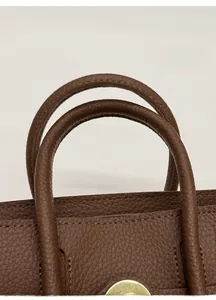 Detailed macro view of the dark brown lychee grain leather handle and fine stitching on the bag