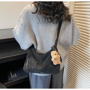 Detail view of black pleated tote bag with plush bear charm on grey knit sweater