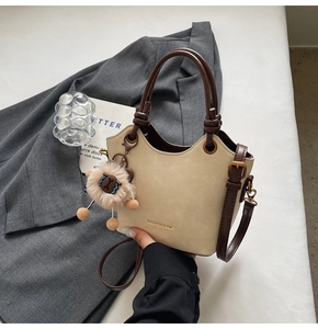 Detail of cream bucket bag with metal logo, brown strap and plush sheep charm on grey blazer