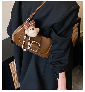 Détail du sac bandoulière en cuir marron foncé avec boucle argentée et breloque ours
