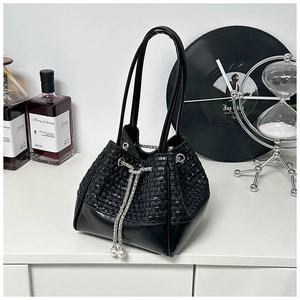 Detail of black drawstring bucket bag with woven texture, silver chain and white pearl accents