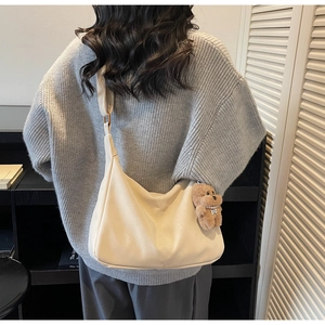 Minimalist beige leather tote bag with a brown bear pendant shown on model's shoulder