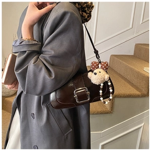 Détail du sac à bandoulière en cuir verni marron avec boucle et breloque ours