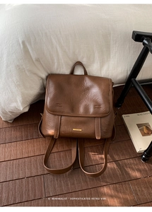 Detailed close-up of brown vintage leather backpack with metal logo on white bedding